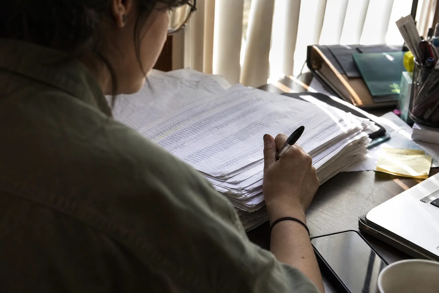 Implementation manager pushing aside printed spreadsheet trackers covered in handwritten fixes
