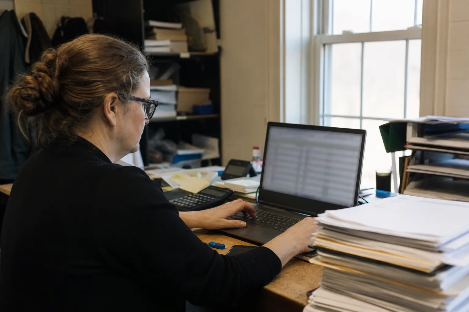 Client office manager filling in a detailed intake form on a laptop with papers beside
