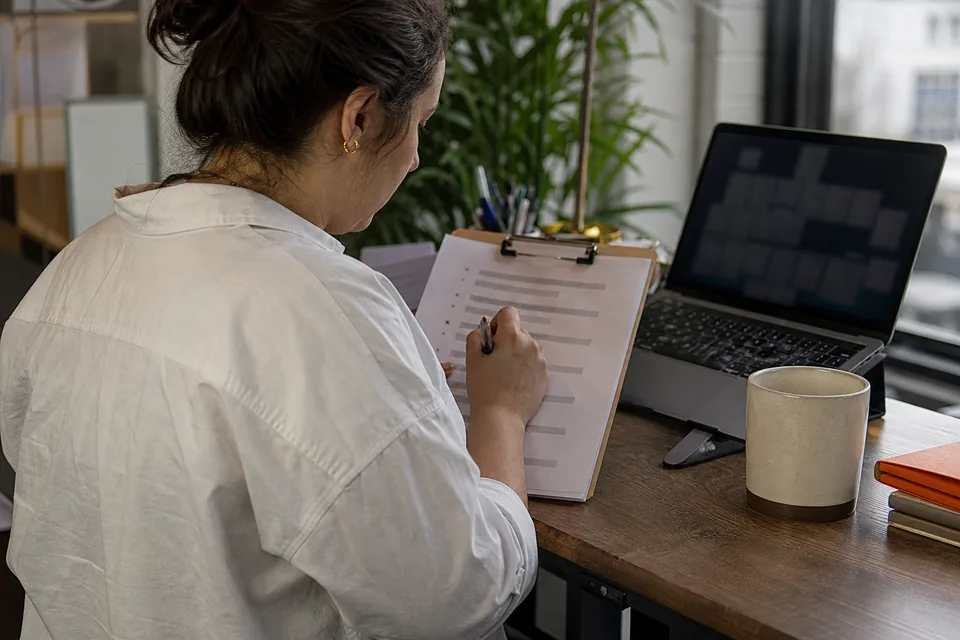 Onboarding lead reviewing a printed go-live checklist with a pen at a standing desk beside a laptop
