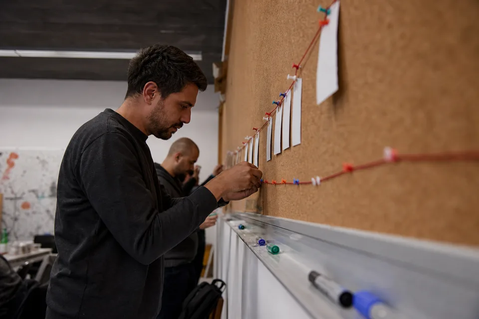 Project lead pinning printed phase cards along a long corkboard timeline