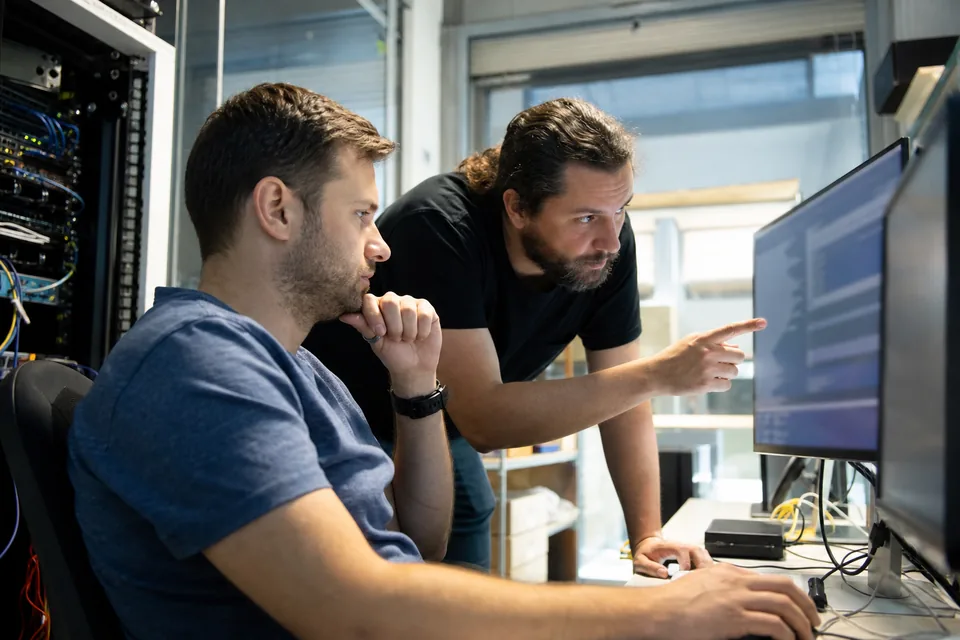 Implementation consultant configuring software settings on a large monitor while a client IT admin watches